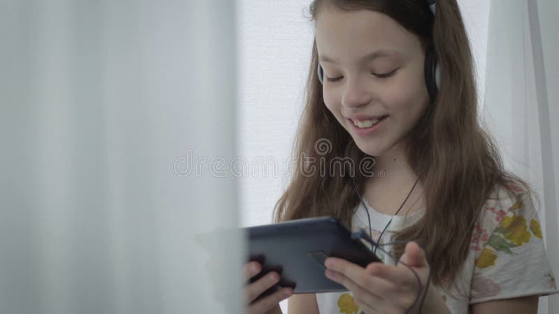 Belle petite fille avec des écouteurs observant les vidéos drôles sur le comprimé et les sourires
