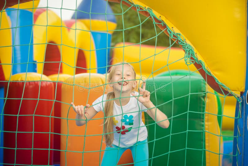 Belle petite fille ayant l'amusement jetant un coup d'oeil par derrière le trempoline gonflable de maille photos stock Belle petite fille ayant l'amusement jetant un coup d'oeil par derrière le trempoline gonflable de maille photos stock