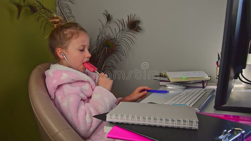 Belle petite fille blonde écoute de la musique sur l'ordinateur et mange des glaces de fruits banque de vidéos