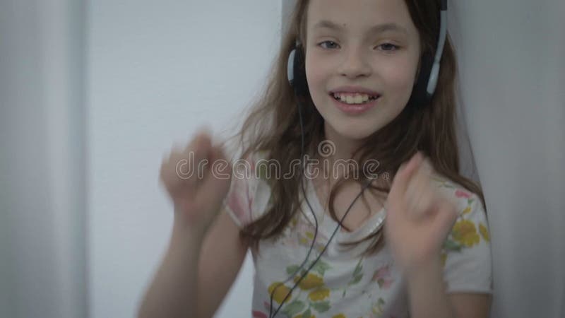 Belle petite fille dans des écouteurs chantant une chanson avec émotion et dansant à la fenêtre