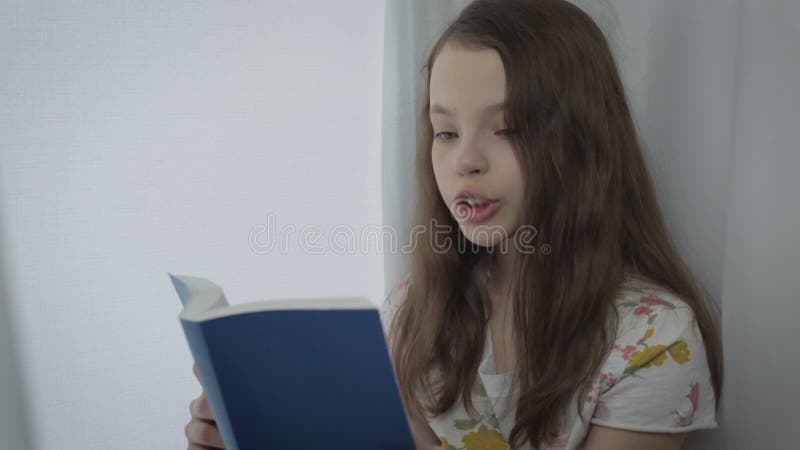 Belle petite fille lisant un livre intéressant par la fenêtre