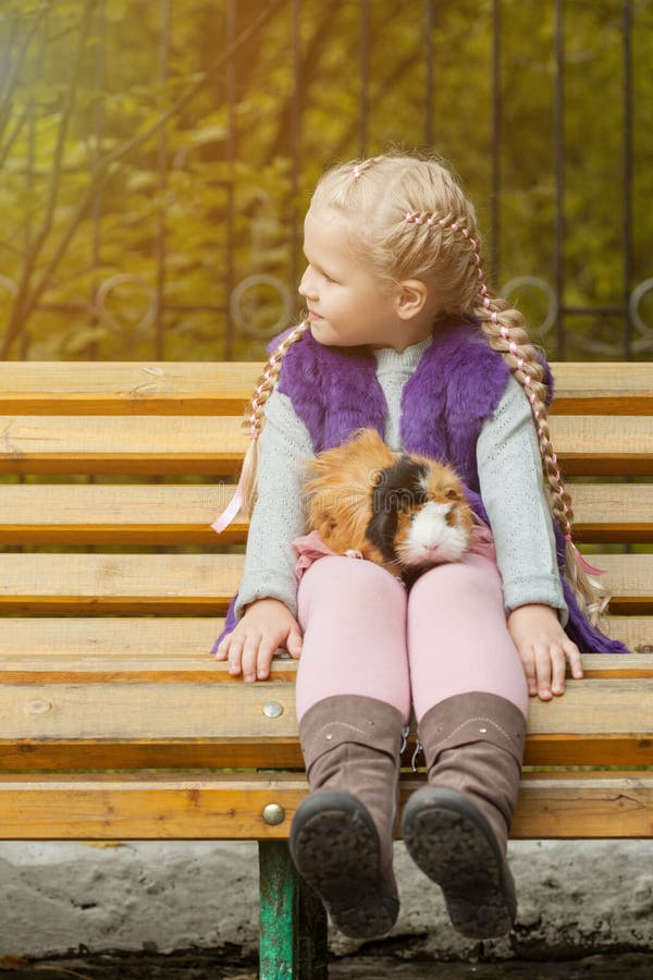 Belle petite fille s'asseyant sur le banc avec son cavy images stock Belle petite fille s'asseyant sur le banc avec son cavy images stock
