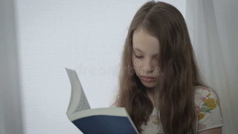 Belle petite fille sérieuse lisant un livre par la fenêtre