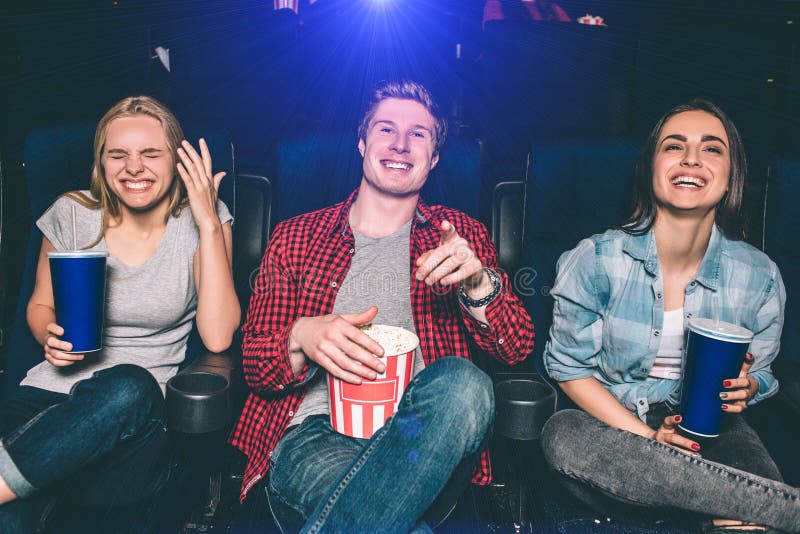 Beautiful picture of happy people laughing in ciname hall. They are looking on screen and smiling. Girls and guy look absolutely stunning and happy. Beautiful picture of happy people laughing in ciname hall. They are looking on screen and smiling. Girls and guy look absolutely stunning and happy