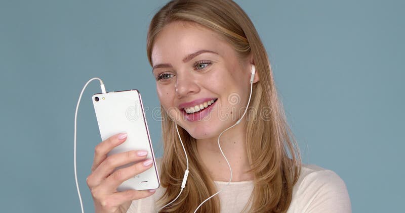 Belle pose heureuse de femme isolé sur la musique d'écoute de mur bleu avec des écouteurs en utilisant le téléphone