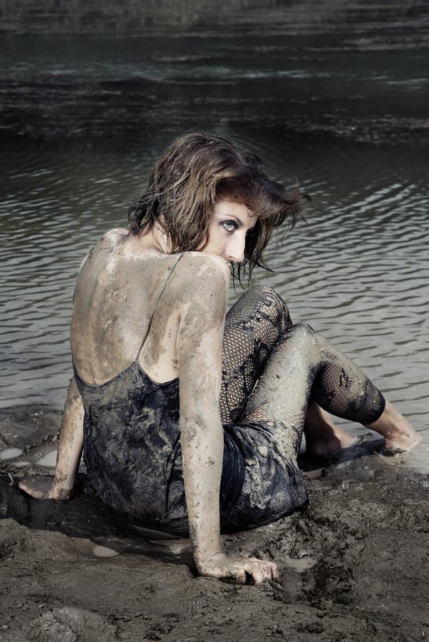 Backview on a woman with dried dirty on her skin sitting at the beach. Backview on a woman with dried dirty on her skin sitting at the beach