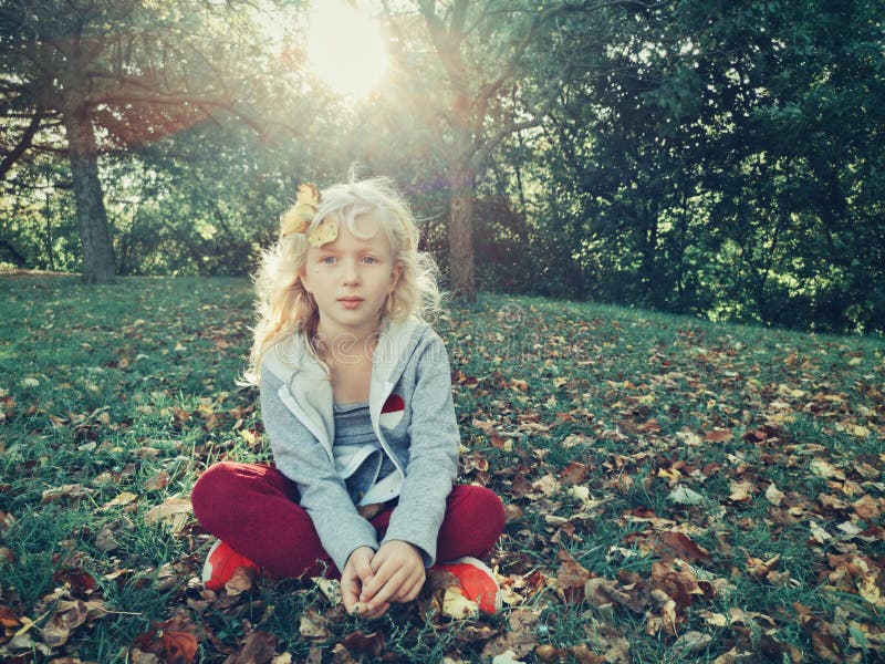 Bellissima bimba bionda caucasica seduta sul prato al parco all'aperto il giorno dell'autunno Ritratto di un bellissimo carino fotografia stock Bellissima bimba bionda caucasica seduta sul prato al parco all'aperto il giorno dell'autunno Ritratto di un bellissimo carino fotografia stock
