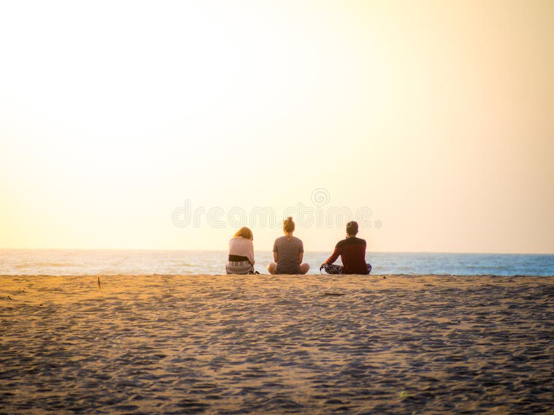 Bellissima foto di due donne e un uomo seduto sulla sabbia a guardare il tramonto sulla spiaggia