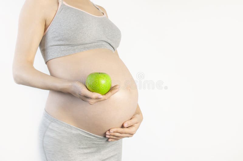 Bellissima giovane donna incinta che tiene in mano una mela verde su fondo bianco Il concetto di aspettativa del bambino, immagine stock libera da diritti Bellissima giovane donna incinta che tiene in mano una mela verde su fondo bianco Il concetto di aspettativa del bambino, immagine stock libera da diritti