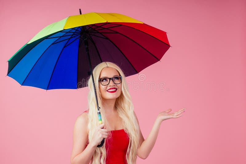 Bellissima giovane donna sorridente con una lunga parrucca bionda con ombrelli colorati sullo sfondo rosa in studio fotografie stock Bellissima giovane donna sorridente con una lunga parrucca bionda con ombrelli colorati sullo sfondo rosa in studio fotografie stock