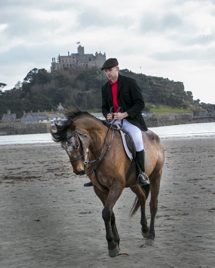 Bello cavallo da equitazione del cavaliere del cavallo maschio sulla spiaggia in abbigliamento tradizionale di guida con il suppo fotografie stock Bello cavallo da equitazione del cavaliere del cavallo maschio sulla spiaggia in abbigliamento tradizionale di guida con il suppo fotografie stock