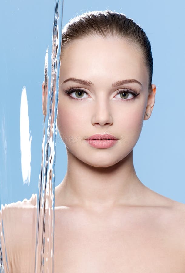 Beautiful young face of woman with clean skin on it and stream of water - blue background. Beautiful young face of woman with clean skin on it and stream of water - blue background