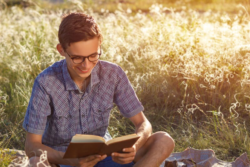Bello giovane tipo felice con i vetri all'aperto che legge un libro un giorno soleggiato fotografia stock Bello giovane tipo felice con i vetri all'aperto che legge un libro un giorno soleggiato fotografia stock