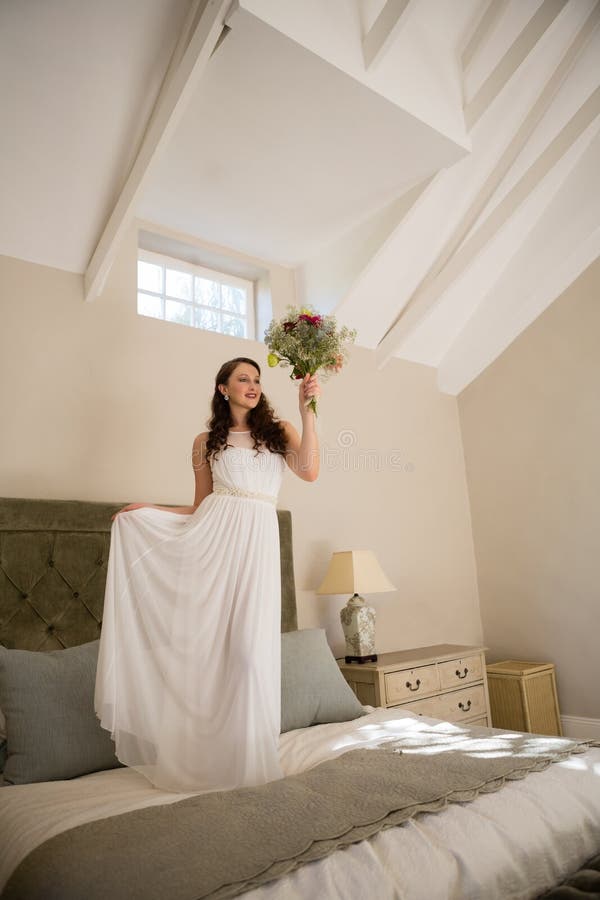 Bello mazzo della tenuta della sposa mentre stando sul letto fotografie stock Bello mazzo della tenuta della sposa mentre stando sul letto fotografie stock
