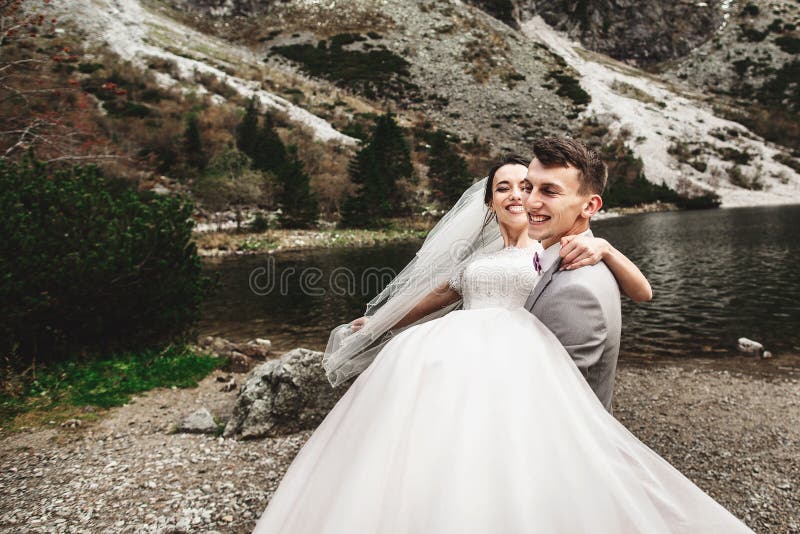 Bello photosession di nozze Lo sposo circonda la sua giovane sposa, sulla riva del lago Morskie Oko poland fotografia stock libera da diritti Bello photosession di nozze Lo sposo circonda la sua giovane sposa, sulla riva del lago Morskie Oko poland fotografia stock libera da diritti