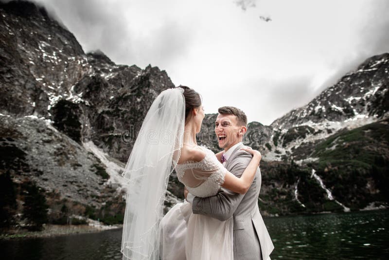 Bello photosession di nozze Lo sposo circonda la sua giovane sposa, sulla riva del lago Morskie Oko poland fotografia stock libera da diritti Bello photosession di nozze Lo sposo circonda la sua giovane sposa, sulla riva del lago Morskie Oko poland fotografia stock libera da diritti
