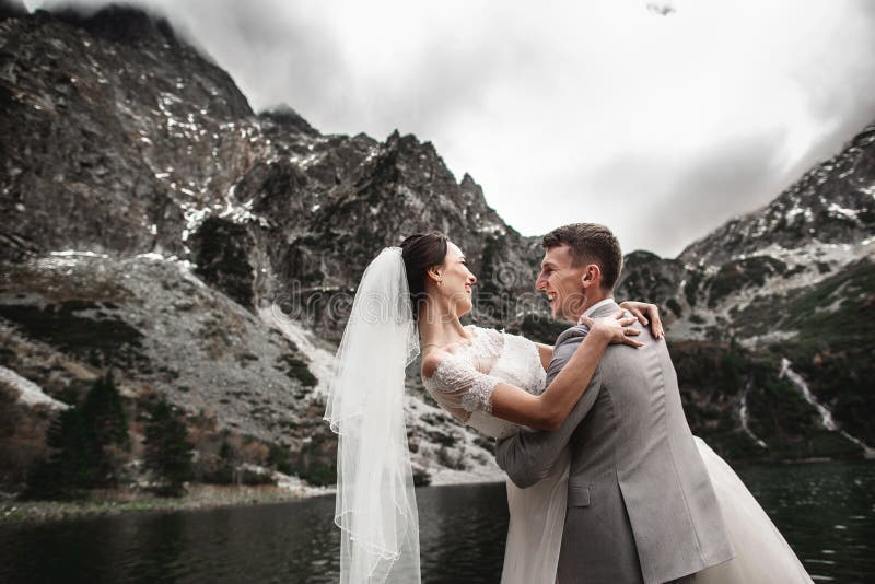 Bello photosession di nozze Lo sposo circonda la sua giovane sposa, sulla riva del lago Morskie Oko poland fotografie stock libere da diritti Bello photosession di nozze Lo sposo circonda la sua giovane sposa, sulla riva del lago Morskie Oko poland fotografie stock libere da diritti