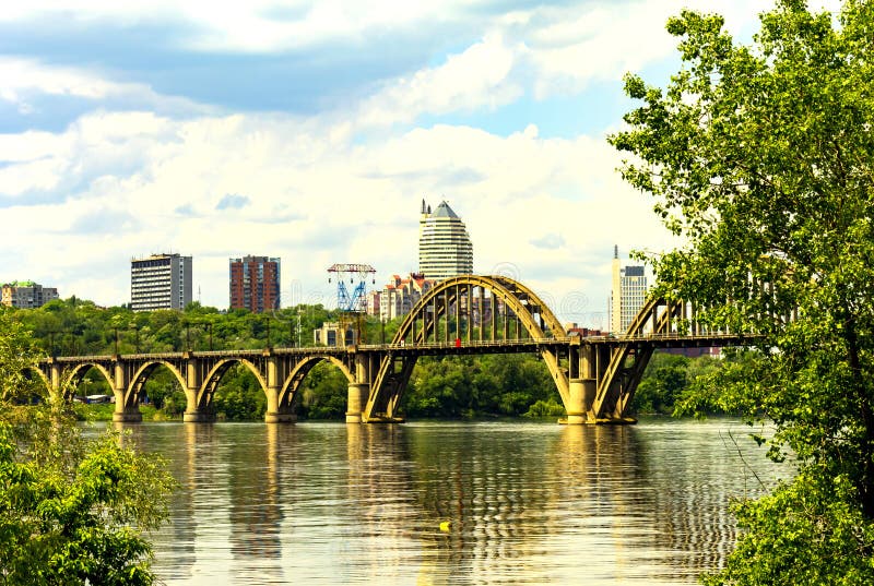 Bello ponte incurvato di Merefoherson sul fiume di Dnieper e una vista dei grattacieli della città di Dnipro immagine stock libera da diritti Bello ponte incurvato di Merefoherson sul fiume di Dnieper e una vista dei grattacieli della città di Dnipro immagine stock libera da diritti