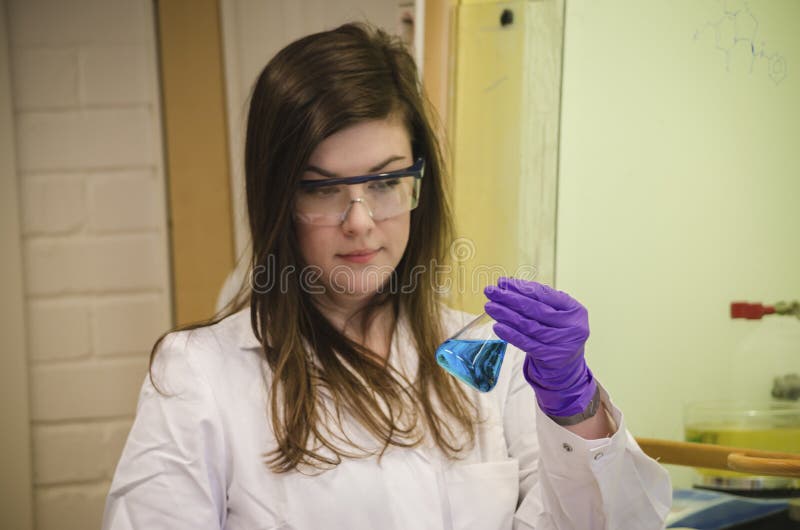 Bello scienziato della donna che tiene e che esamina una soluzione blu nel laboratorio di chimica immagine stock libera da diritti Bello scienziato della donna che tiene e che esamina una soluzione blu nel laboratorio di chimica immagine stock libera da diritti