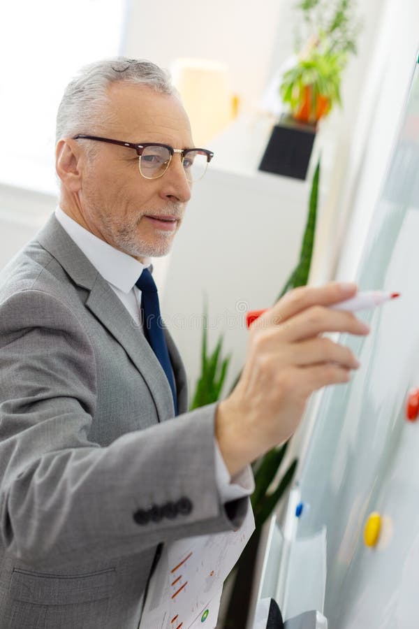 Bello tipo anziano piacevole in costume grigio che redige informazioni per i lavoratori fotografie stock libere da diritti Bello tipo anziano piacevole in costume grigio che redige informazioni per i lavoratori fotografie stock libere da diritti