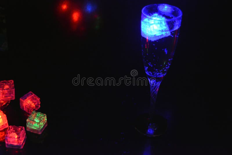 Bello y brillante cubo de hielo azul flotante en una copa de champán de vidrio con una bebida. imagen de archivo