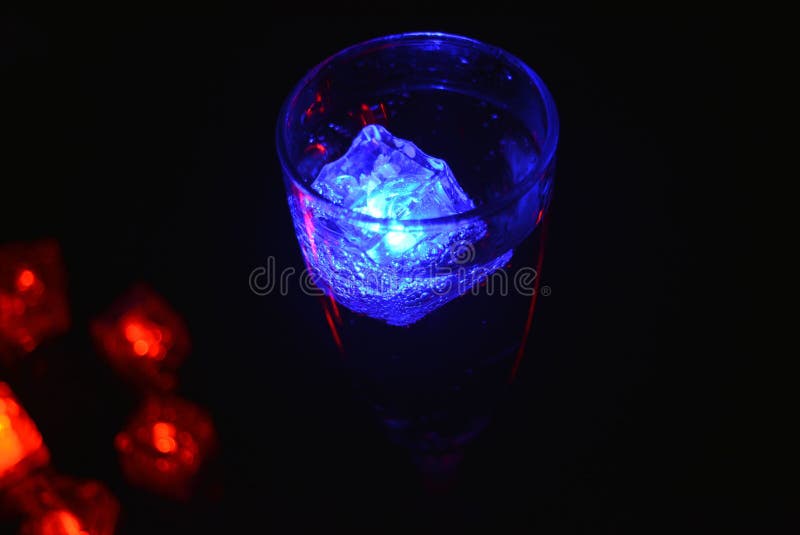 Bello y brillante cubo de hielo azul flotante en una copa de champán de vidrio con una bebida. imagen de archivo