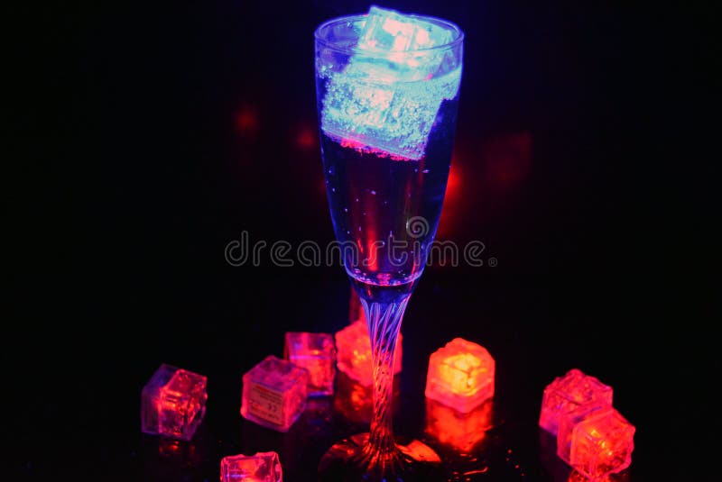 Bello y brillante cubo de hielo azul flotante en una copa de champán de vidrio con una bebida. imagen de archivo
