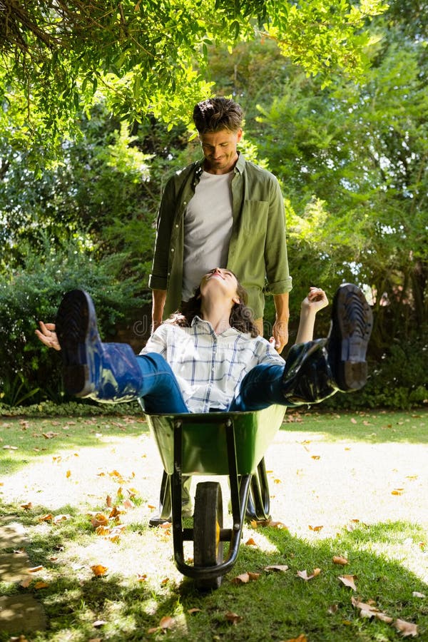 Bemannen Sie das Einwirken auf Frau beim Druck der Schubkarre im Garten stockfotos Bemannen Sie das Einwirken auf Frau beim Druck der Schubkarre im Garten stockfotos