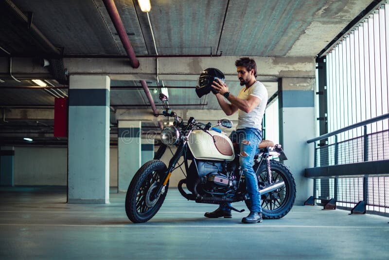 Bemannen Sie das Setzen auf Motorradsturzhelm in eine Garage stockbild Bemannen Sie das Setzen auf Motorradsturzhelm in eine Garage stockbild