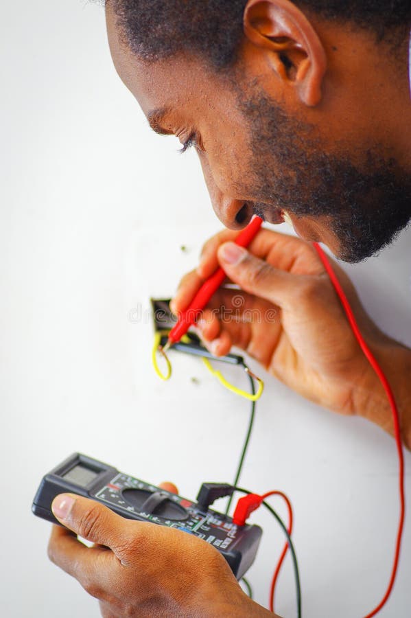 Bemannen Sie das Tragen des weißen und blauen Hemdes, das an elektrischen Wandsteckdosedrähten unter Verwendung des Vielfachmessg lizenzfreies stockbild Bemannen Sie das Tragen des weißen und blauen Hemdes, das an elektrischen Wandsteckdosedrähten unter Verwendung des Vielfachmessg lizenzfreies stockbild