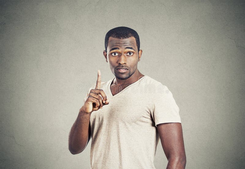 Closeup portrait young man pointing up having idea, solution, showing with index finger number one isolated grey wall background. Closeup portrait young man pointing up having idea, solution, showing with index finger number one isolated grey wall background.