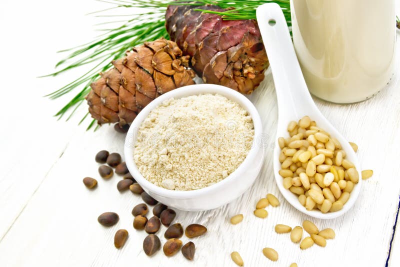 Cedar flour in a bowl, nuts and cones, a spoon with peeled nuts, pine branch and cedar milk in a bottle on wooden board background. Cedar flour in a bowl, nuts and cones, a spoon with peeled nuts, pine branch and cedar milk in a bottle on wooden board background
