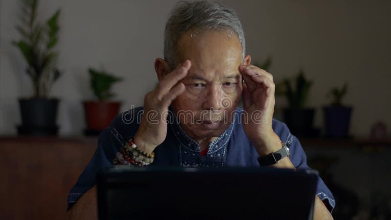 Bemoeide aziatische oudere man zit aan de werkplek en haalt de ogen van de laptop af en masseert de tempels om vermoeidheid te ver