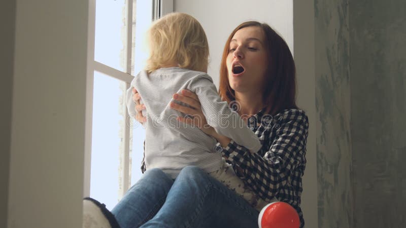 Bemuttern Sie Spiele mit ihrem kleinen Baby nahe dem Fenster