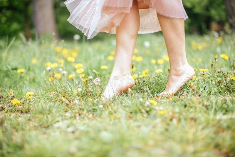 Ben av unga barfota kvinnor som bär den rosa klänningen som står på ett ben på grönt gräs med gula blommor, slut upp royaltyfri fotografi Ben av unga barfota kvinnor som bär den rosa klänningen som står på ett ben på grönt gräs med gula blommor, slut upp royaltyfri fotografi