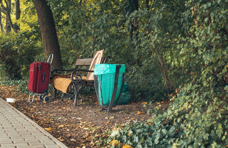 Bench in autumn park with sutitcase and homeless stuffs.