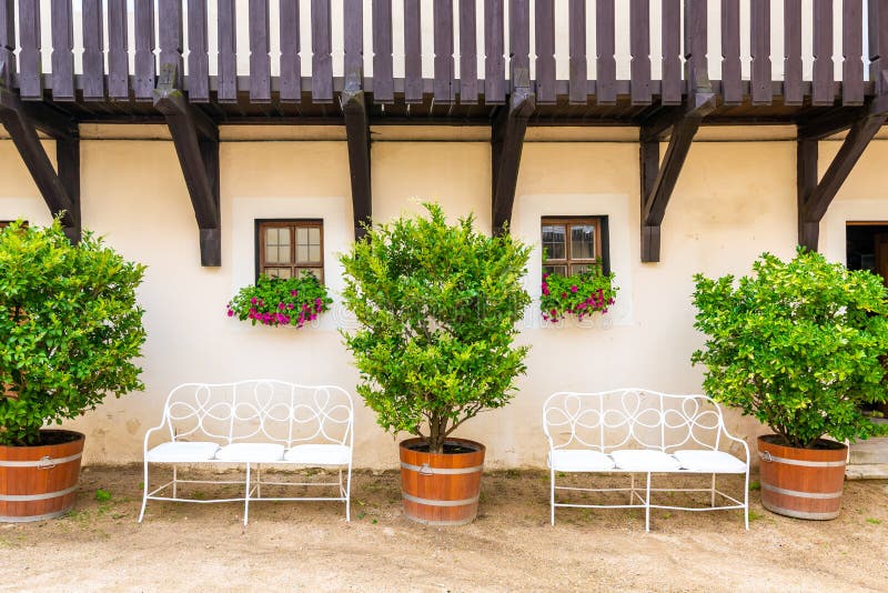 Bench under the window with flower. Big bushes next to the bench with fresh green leaves. Old home building in Europe, vintage royalty free stock images Bench under the window with flower. Big bushes next to the bench with fresh green leaves. Old home building in Europe, vintage royalty free stock images