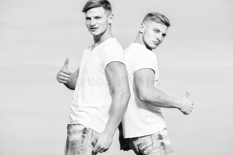 Men twins brothers muscular guys in white shirts sky background. 