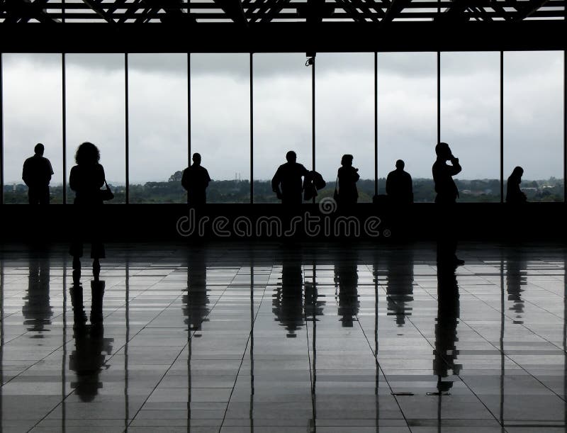 Silhouetted people against the windows of an airport observation deck. The greyish floor and clouded day gives it a very monochrome aspect. Silhouetted people against the windows of an airport observation deck. The greyish floor and clouded day gives it a very monochrome aspect.