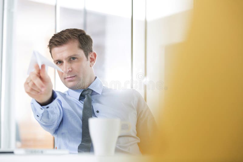 Bepaalde zakenman die document vliegtuig in bureau werpen stock fotografie Bepaalde zakenman die document vliegtuig in bureau werpen stock fotografie
