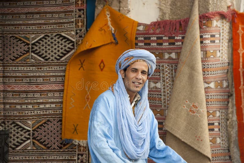 Berber man with turban in front of colorful carpets, Morocco