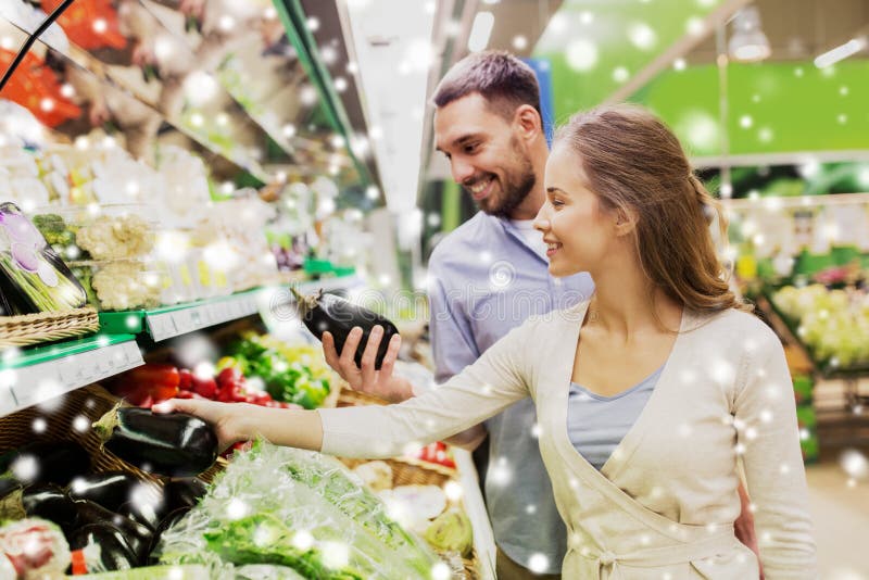 Berenjena de compra de los pares felices en el colmado. Compras, comida, venta, consumerismo y concepto de la gente - aguacate de compra de los pares felices en el colmado o el supermercado sobre nieve