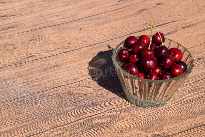 Berries of a sweet cherry in a glass bowl on a wooden background. Ripe red sweet stock photo Berries of a sweet cherry in a glass bowl on a wooden background. Ripe red sweet stock photo
