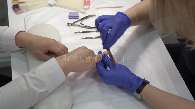 Berufsmanikürist in den Handschuhen, die Fingernägel vor der Abdeckung mit Lack polieren