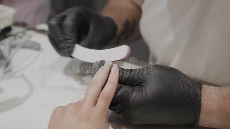 Berufsmaniküristmann poliert und macht die Nägel des Mädchens mit einer Nagelfeile glatt