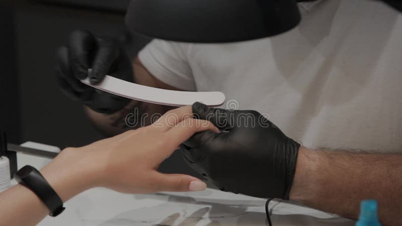 Berufsmaniküristmann poliert und macht die Nägel des Mädchens mit einer Nagelfeile glatt