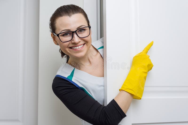 Berufsreinigungsservice Die Frauenhausgehilfin in den gelben Gummihandschuhen zeigend mit einem Finger auf die weiße Tür ist der lizenzfreies stockfoto