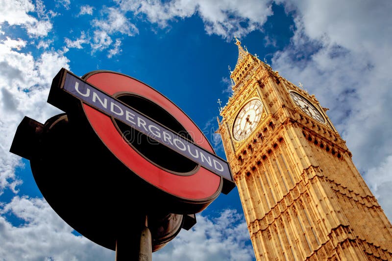 Famous London underground sign and Westminster Parliament on blue sky with clouds. Famous London underground sign and Westminster Parliament on blue sky with clouds