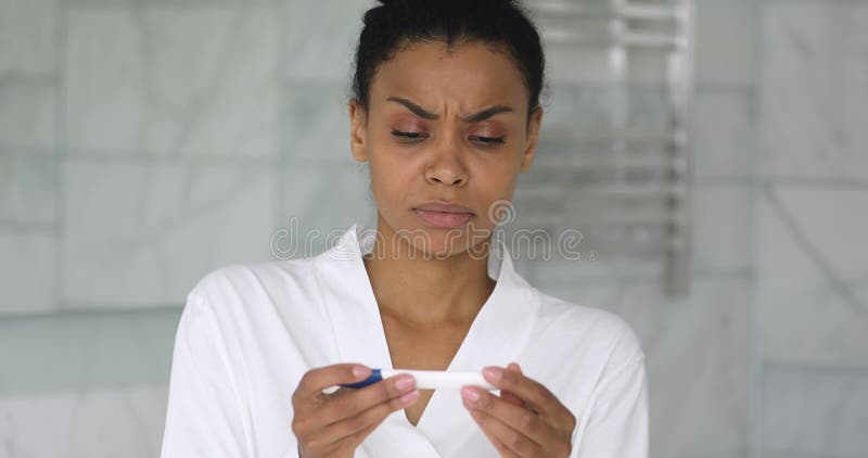 Berörd, stressad ung afrikansk amerikan-flicka som håller ett graviditetstest.