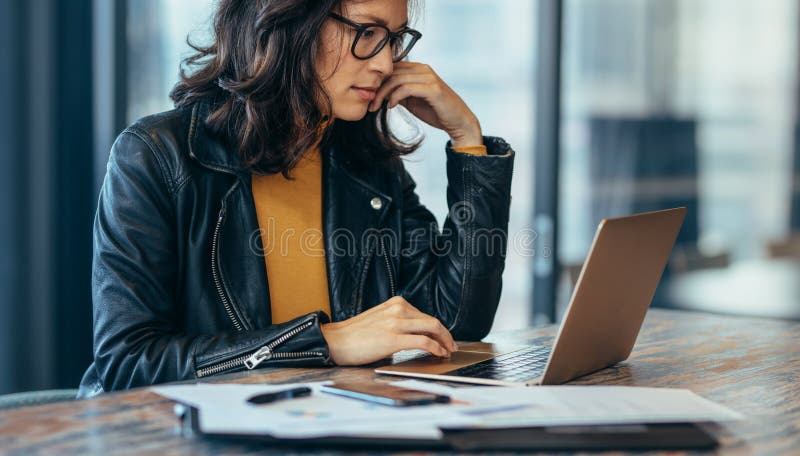 Beschäftigte Frau, die auf Schreibtisch sitzt und an Laptop arbeitet